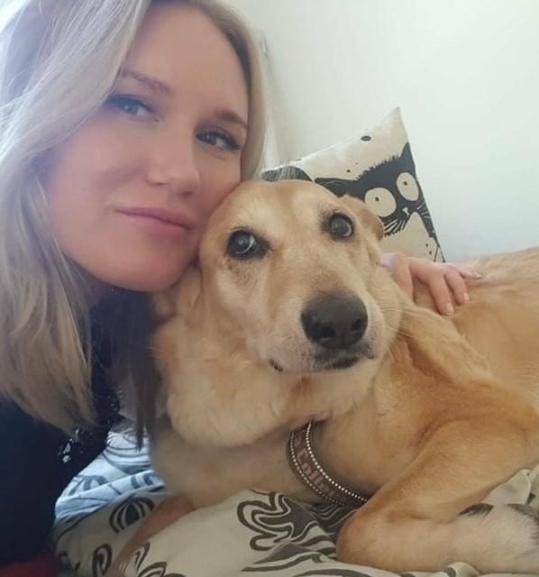 Jenna Hovinen, geronomi harjoitelija. Nuori vaaleatukkainen nainen halaamassa isoa koiraa.