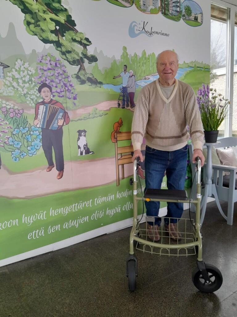 Iäkäs mies seisoo rollaattorin kanssa.