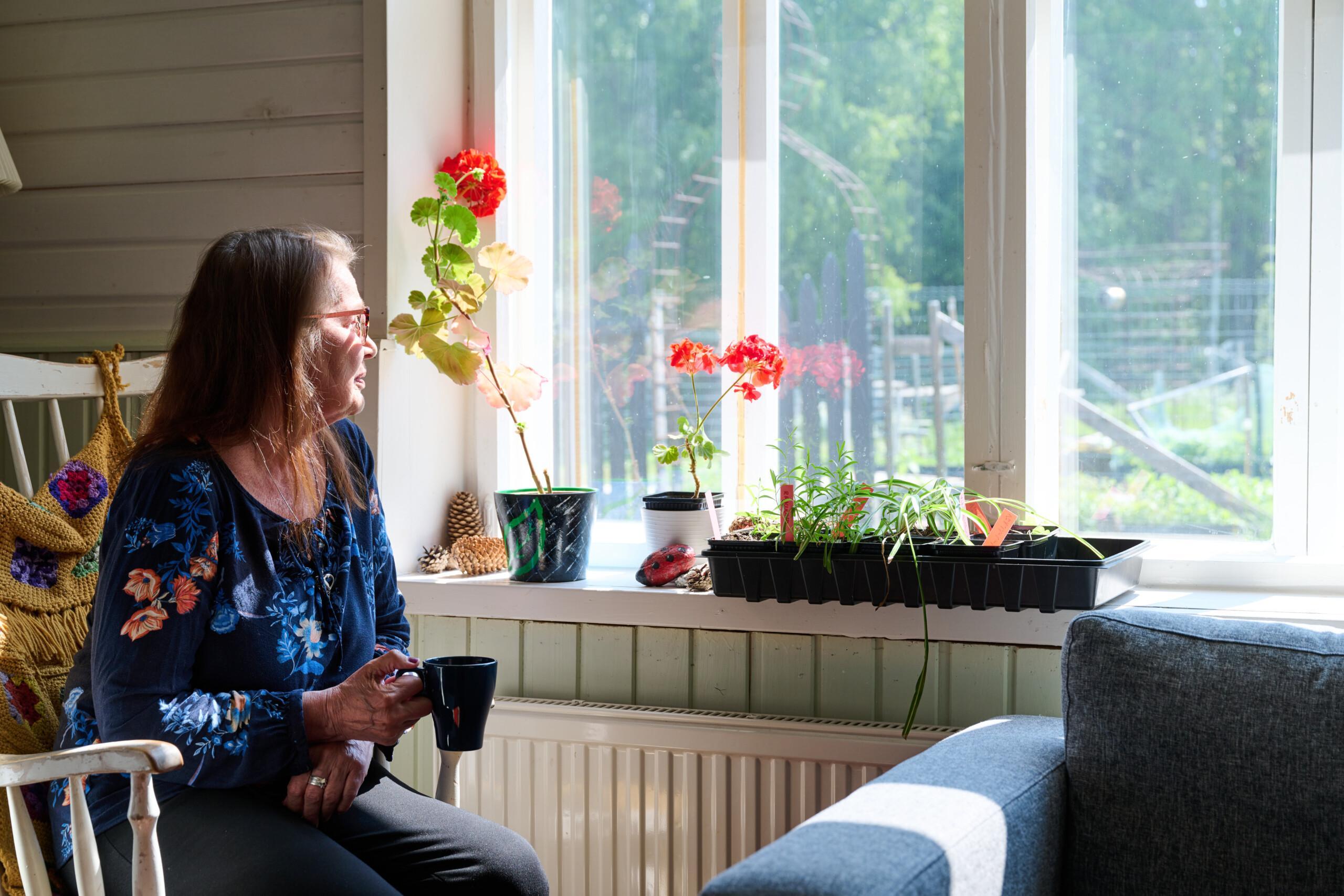 Ensam kvinna sitter vid fönstret och tittar ut.