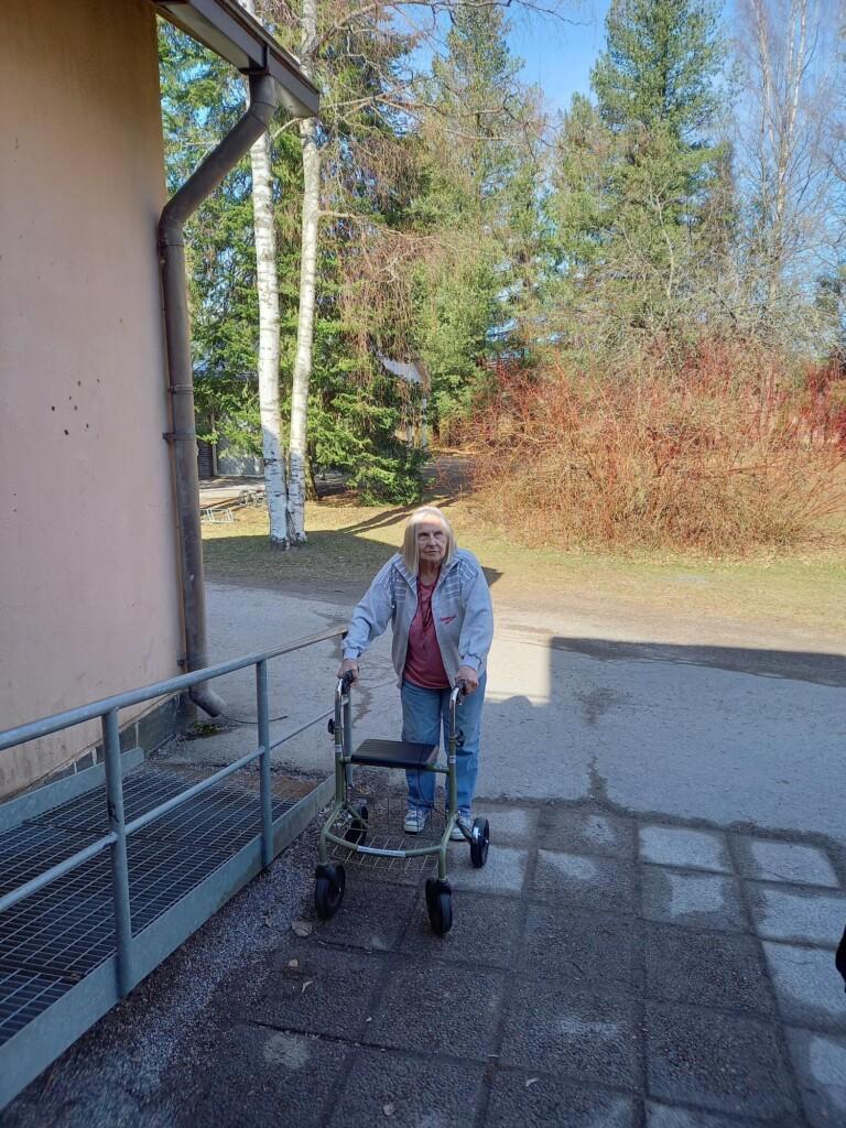 Iäkäs nainen rollaattorin kanssa ulkona. 