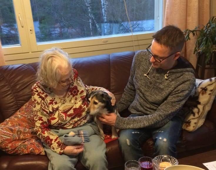 Vanha nainen silittää sohvalla koiraa.