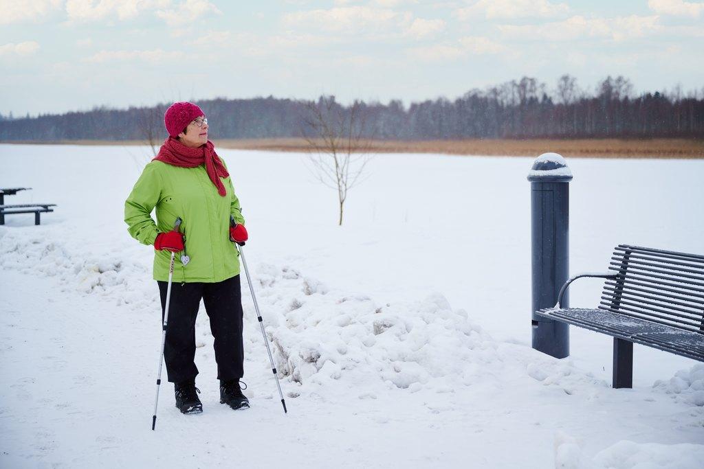 Vanha nainen seisoo talvisessa maisemassa kävelysauvoihin nojaten.
