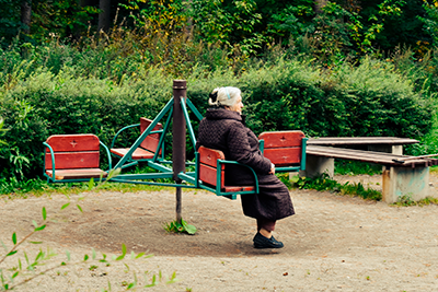 Vanha nainen istuu yksin puistossa lasten karusellissa.