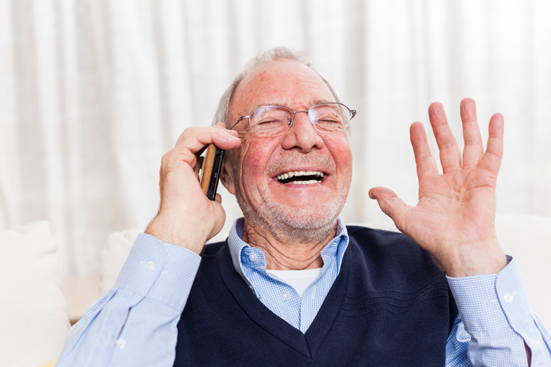 En gammal man pratar i telefon och skrattar.