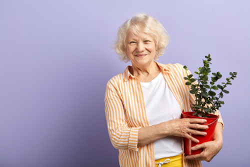 En gammal kvinna tittar på kameran och håller en blomkruka i sitt knä.