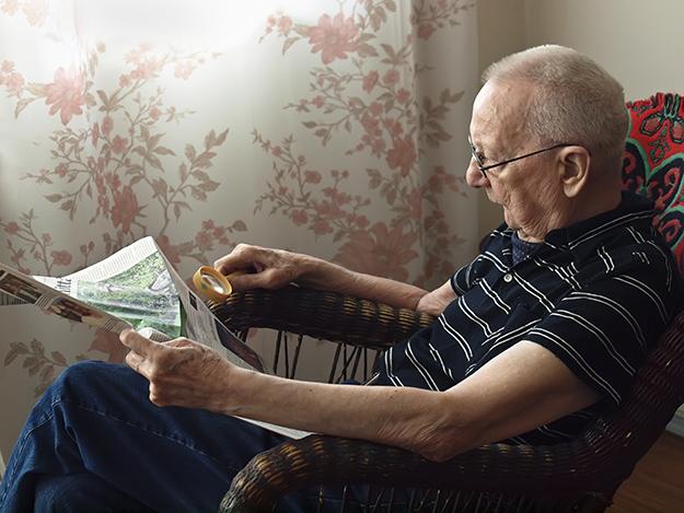 En gammal man sitter och läser en tidning inomhus.