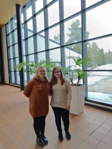 Kaksi nuorta naista seisoo koulun aulassa ison ikkunan edessä. 