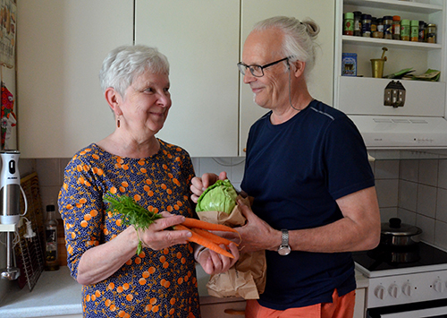 Iäkäs pariskunta seisoo keittiössä vihanneksiä kädessä ja katsovat toisiinsa.