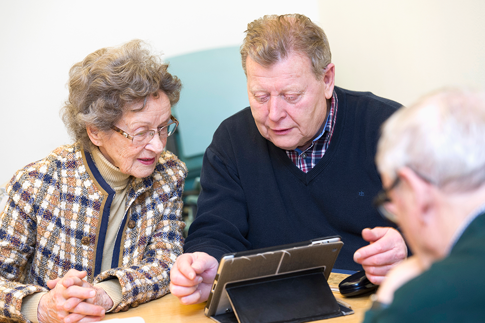 Tre gamla människor söker information på tabletten.
