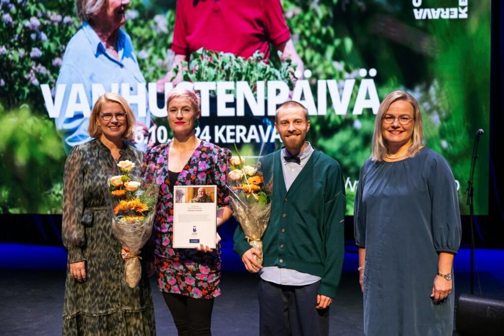 Kolme keski-ikäistä naista ja yksi mies poseeraavat lavalla kameralle. 