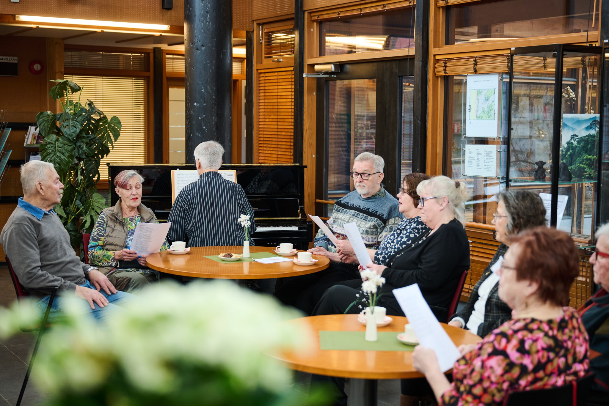 Yhteislaulu tilaisuus Hyvinvointikeskus Onnin aulassa. Iäkkäitä laulamassa ja mies säestää pianolla.