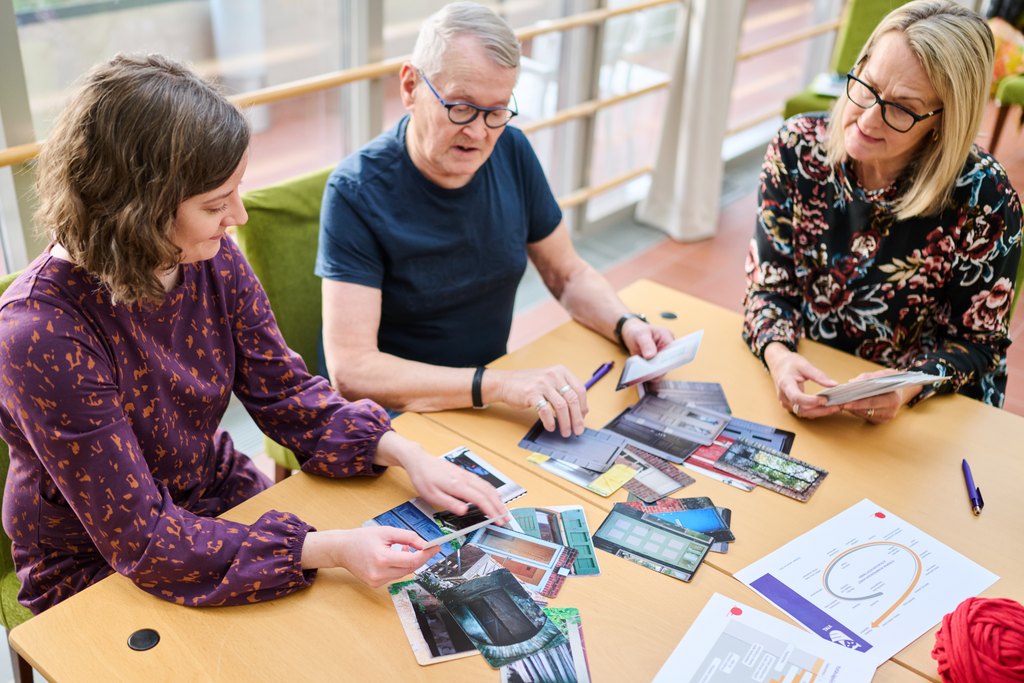 Kolme henkilöä keskustelevat pöydän äärellä kuvista.
