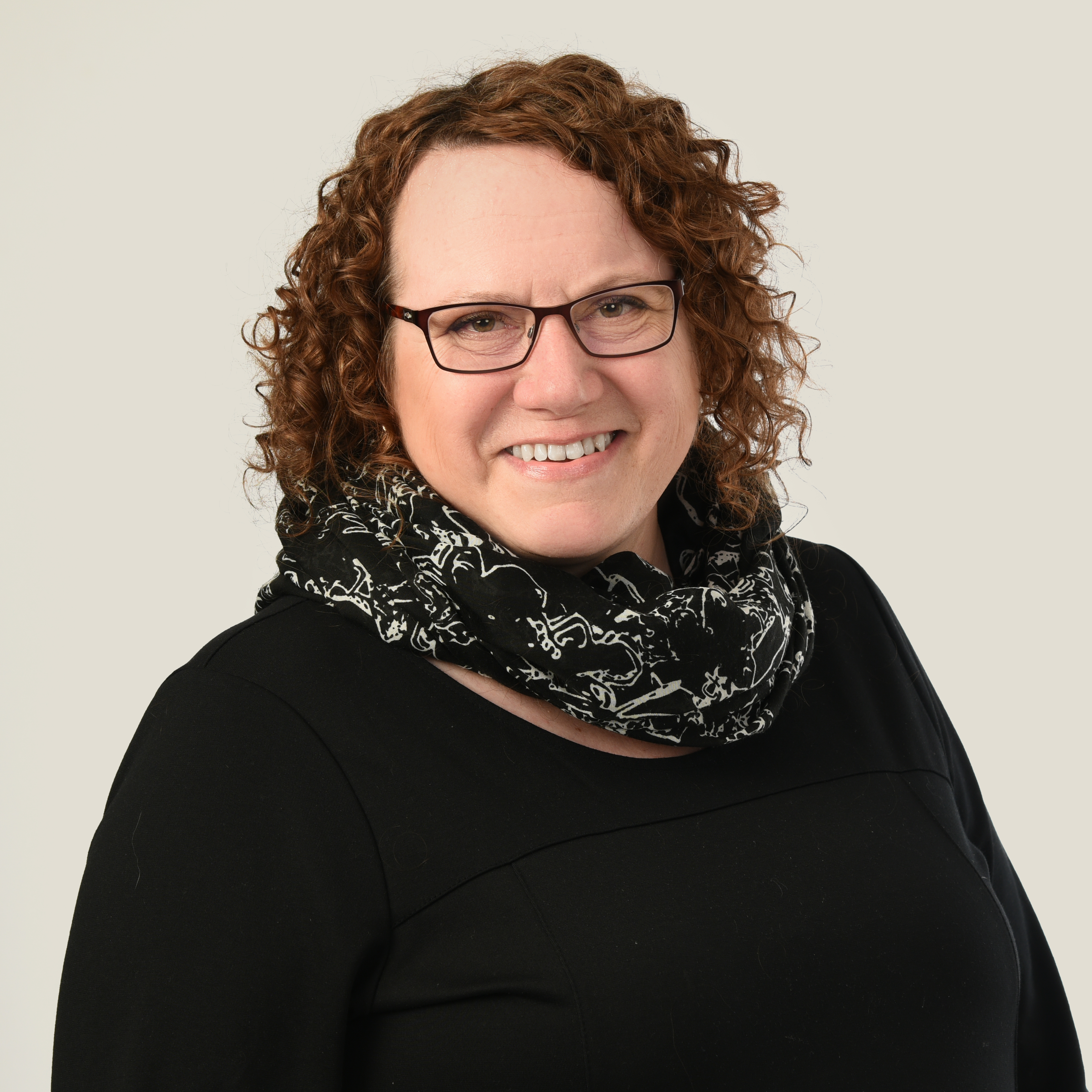 Keski-ikäinen nainen. Tummat hiukset, silmälasit ja mustat vaatteet.