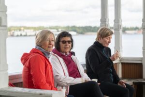 Kolme iäkästä henkilöä nauttimassa kahvista ulkopenkillä.