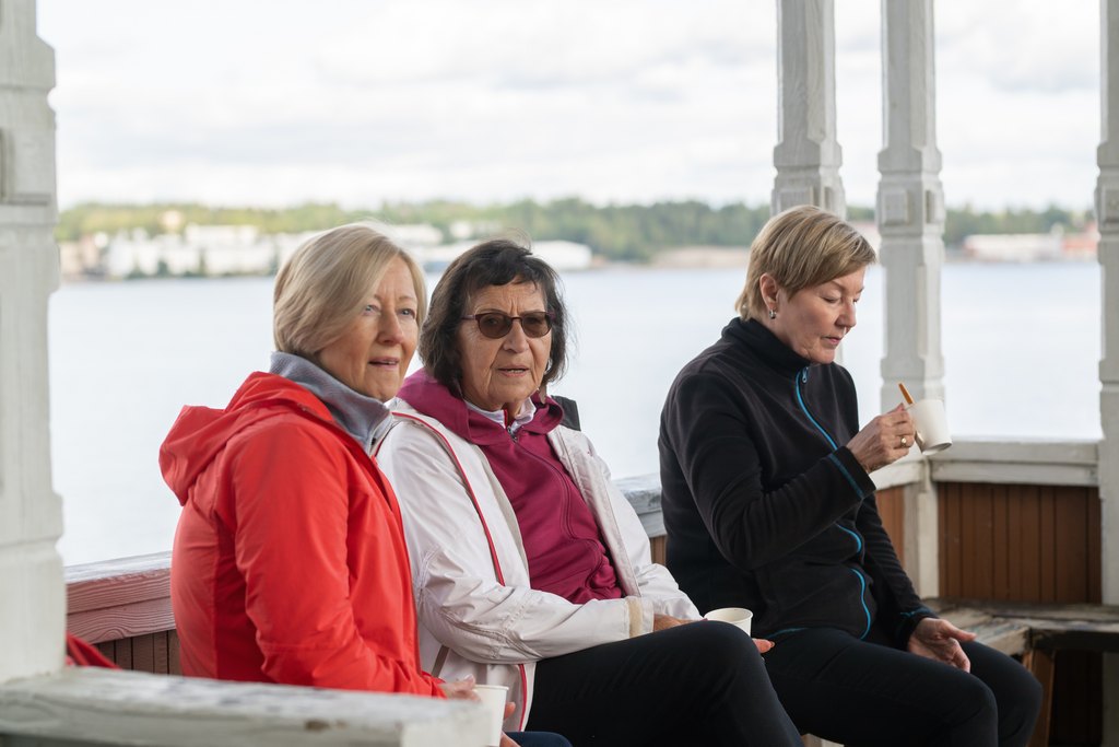 Kolme iäkästä henkilöä nauttimassa kahvista ulkopenkillä.