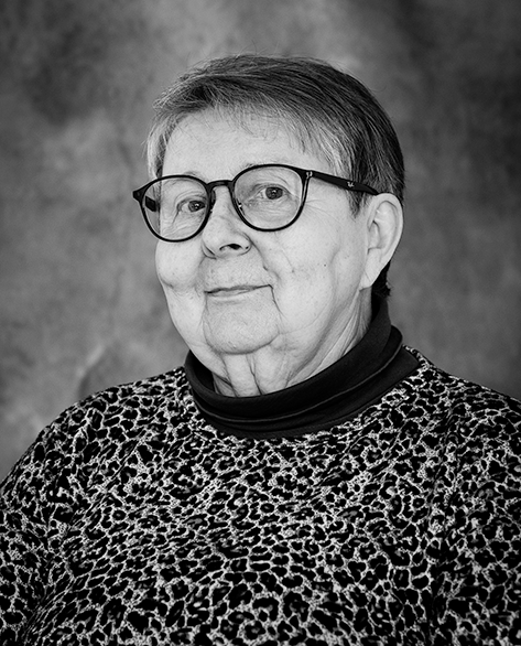 Mustavalkoinen muotokuva iäkkäästä naisesta, jolla on lyhyet hiukset ja silmälasit. Hänellä on yllään leopardikuvioinen paita ja musta poolokaulus. Taustalla on yksivärinen studiotausta.