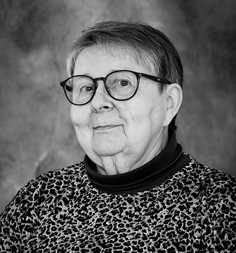 Mustavalkoinen muotokuva iäkkäästä naisesta, jolla on lyhyet hiukset ja silmälasit. Hänellä on yllään leopardikuvioinen paita ja musta poolokaulus. Taustalla on yksivärinen studiotausta.