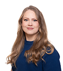 Värillinen muotokuva nuoresta aikuisesta, jolla on pitkät vaaleat hiukset ja sininen pusero. Hän katsoo kameraan ja hymyilee hillitysti valkoista taustaa vasten.