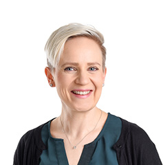 Vaaleahiuksinen henkilö katsoo kameraan ja hymyilee. Hänellä on yllään vihreä paita ja tumma neuletakki, ja tausta on neutraali.