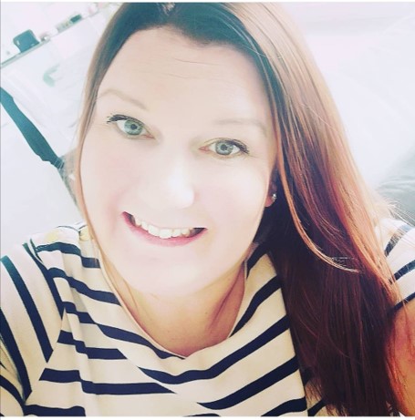 Pitkähiuksinen nainen ottaa itsestään lähikuvan ja hymyilee. Hänellä on tummanruskeat hiukset ja yllään raidallinen paita. Kuva on otettu sisätiloissa luonnonvalossa.