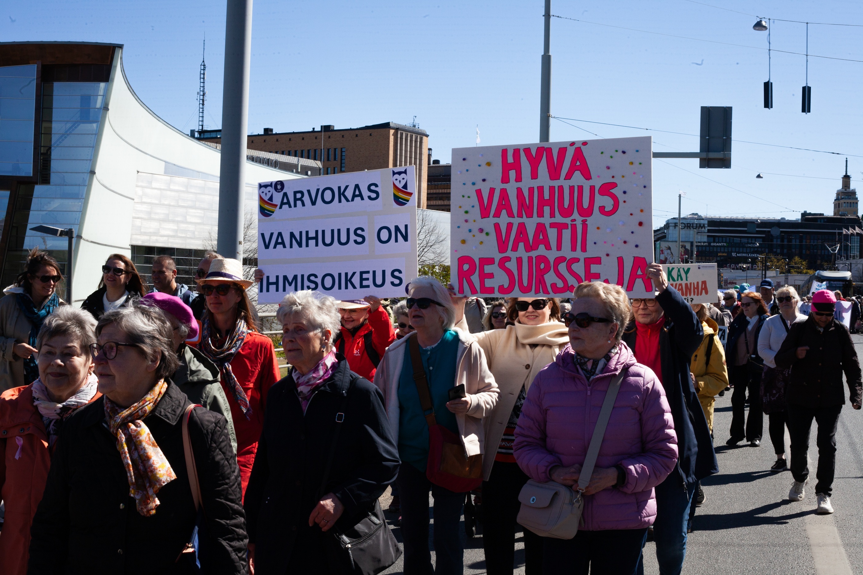 Iäkkäitä ihmisiä marssii kaupungin keskustassa kylttien kanssa. Kylteissä lukee ”Arvokas vanhuus on ihmisoikeus” ja ”Hyvä vanhuus vaatii resursseja”.